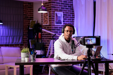Vlogger recording internet show using modern camera, talking about international news and events subjects. Man filming live broadcast using professional gadgets in rgb lights studio