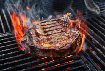Barbecue dry aged wagyu prime rib beef steak grilled as close-up on a charcoal grill with fire and smoke