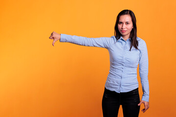 Displeased asian woman showing dislike gesture on camera in studio, gesturing disagreement sign...