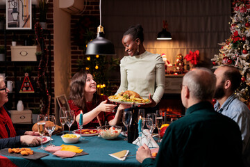 Persons enjoying christmas eve dinner at home with festive decorations and xmas tree near fireplace. Family and friends celebrating winter holiday season with traditional food.