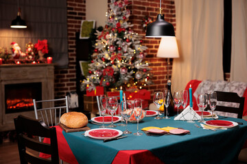 Decorated christmas tree and ornaments near festive dinner table to celebrate seasonal december holiday with family and friends. Dinning party event with traditional meal and wine.