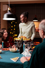 People celebrating christmas eve together with festive dishes and wine, enjoying winter seasonal event with family. Men and women meeting near fireplace to celebrate traditional day with xmas tree.