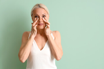 Mature woman doing face building exercise on green background