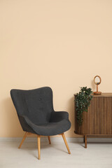 Dark grey armchair with dresser, mirror and houseplant near beige wall