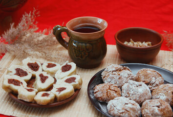 Homemade baked goods - handmade grilled cookies, chopped dumplings, nuts, clay cup of tea on a red background.