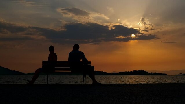 Family after quarrel by sea. A view of man and woman silhouette sitting on bench after family quarrel. A concept of divorce problems in the couple.
