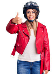 Young beautiful woman wearing motorcycle helmet smiling happy and positive, thumb up doing excellent and approval sign