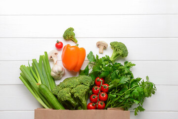 Paper bag with fresh vegetables, mushrooms and greenery on white wooden background