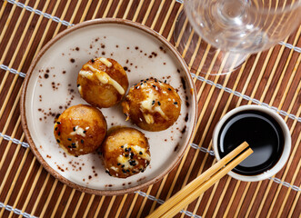 On wooden table plate with takoyaki - crispy fried dough balls containing octopus and other seafood. Popular hearty Japanese dish, restaurant menu, fast food offers.