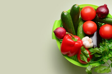 Colander with fresh vegetables and greenery on light green background