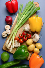 Wooden board with fresh vegetables, fruits and mushrooms on blue background