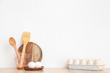 Kitchen utensils and eggs on wooden table near white wall
