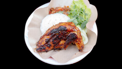 Grilled chicken rice, chili sauce, cucumber, basil leaves, lettuce leaves and chili sauce on a plate, black background