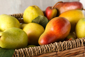 Wicker box with ripe pears on grey background