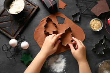 Woman preparing tasty Christmas gingerbread cookies on black background