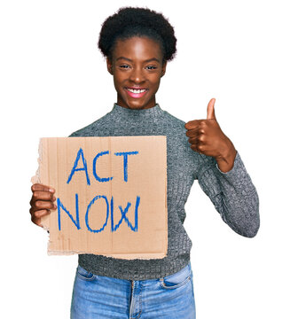 Young african american girl holding act now banner smiling happy and positive, thumb up doing excellent and approval sign