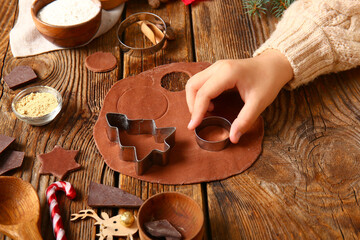 Woman preparing tasty Christmas gingerbread cookies on brown wooden background