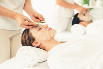 Serene daylight ambiance of spa salon, couple customer indulges in rejuvenating with luxurious cucumber facial mask. Facial skincare treatment and beauty care concept. Quiescent