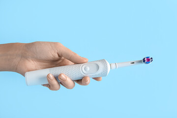 Female hand with electric toothbrush on blue background.