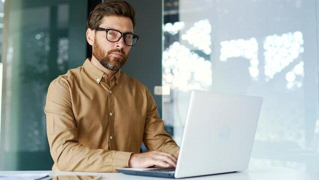 Serious thoughtful manager works on a laptop while sitting at a workplace in a business office. Entrepreneur is thinking about solving a problem, busy with a startup project, banking in computer app