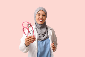 Female Muslim doctor in hijab with stethoscope on pink background. World Hijab Day concept