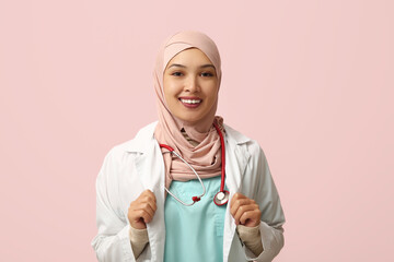 Female Muslim doctor in hijab with stethoscope on pink background. World Hijab Day concept