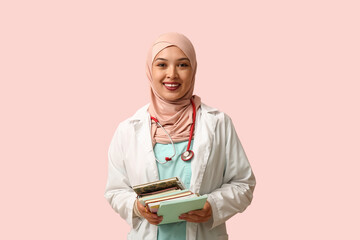 Fototapeta premium Female Muslim doctor in hijab with journals on pink background. World Hijab Day concept