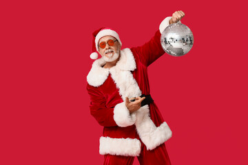 Santa Claus in sunglasses pointing at disco ball on red background