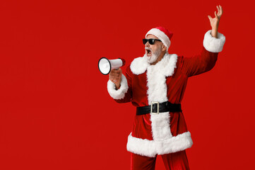 Santa Claus in sunglasses with megaphone screaming on red background