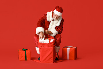 Santa Claus with bag full of gift boxes sitting on red background