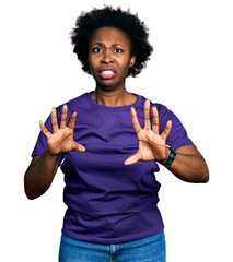 African american woman with afro hair wearing casual purple t shirt afraid and terrified with fear...