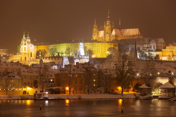 Fototapeta na wymiar The night snowy Prague Lesser Town with gothic Castle and Charles Bridge above River Vltava, Czech Republic