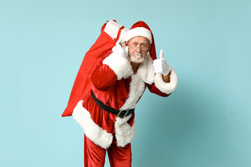 Fototapeta na wymiar Santa Claus with bag full of gift boxes showing thumb-up gesture on blue background
