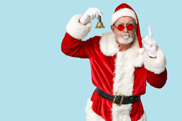 Santa Claus in sunglasses with Christmas bell pointing at something on blue background