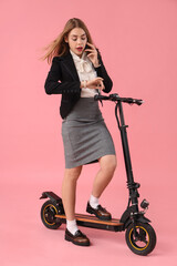 Portrait of panicked businesswoman talking by phone while riding kick scooter on pink background