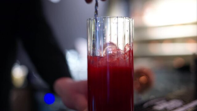 Barman making a red lemonade cocktail with ice at a bar