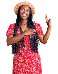 Young african american woman wearing summer hat smiling swearing with hand on chest and fingers up, making a loyalty promise oath