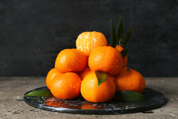 Board with sweet mandarins and leaves on grey table