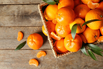 Wicker basket with sweet mandarins and leaves on wooden background