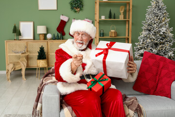 Obraz premium Santa Claus with gift boxes celebrating Christmas on sofa at home