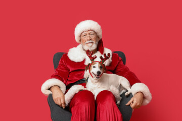 Santa Claus with cute Jack Russell Terrier dog in reindeer horns on red background