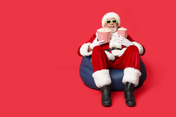 Happy Santa Claus in 3D glasses with buckets of tasty popcorn on red background