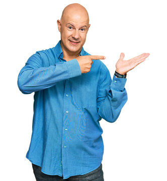 Middle age bald man wearing casual clothes amazed and smiling to the camera while presenting with hand and pointing with finger.