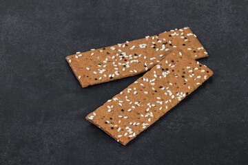 Buckwheat bread with sesame seeds and quinoa, in the form of thin strips. Dark gray background. Close up