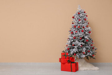 Beautiful decorated Christmas tree with gifts near beige wall