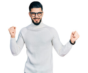 Naklejka premium Young arab man with beard wearing elegant turtleneck sweater and glasses dancing happy and cheerful, smiling moving casual and confident listening to music