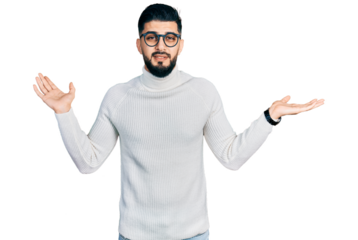 Young arab man with beard wearing elegant turtleneck sweater and glasses clueless and confused expression with arms and hands raised. doubt concept.