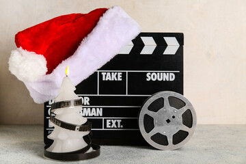 Movie clapper with Santa hat, film reel and candle on light grunge background