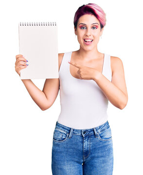 Young beautiful woman with pink hair holding notebook smiling happy pointing with hand and finger