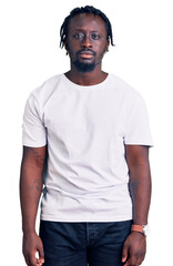 Fototapeta premium Young african american man with braids wearing casual white tshirt relaxed with serious expression on face. simple and natural looking at the camera.